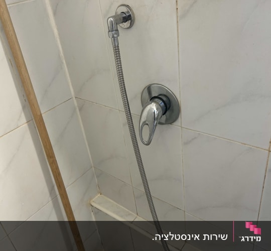 ברז מקלחת עם צינור ומגב על קיר אריחים
